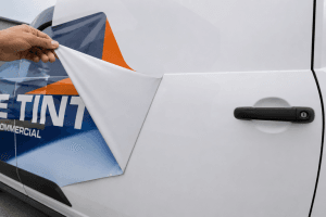 Vinyl vehicle graphic being peeled cleanly from a white van door showing no paint fading or marks underneath